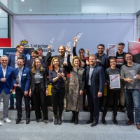 Menschen stehen aufgereiht vor eine Bühne um ein Foto zu machen. Manche von Ihnen halten einen Preis oder eine Urkunde hoch.