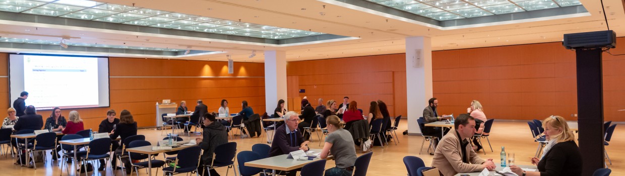 Eine Veranstaltung auf der Leipziger Buchmesse im Congress Center Leipzig. Im Raum stehen mehrere Tische an denen verschieden viele Personen sitzen. 