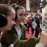 Zwei Mädchen hören Hörbücher an einem Messestand auf der Leipziger Buchmesse. 