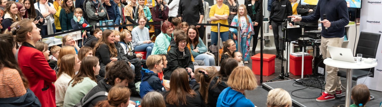 Zahlreiche Kinder und Jugendliche verfolgen eine Lesung in der Messe-Kinderbuchhandlung von Hugendubel. 