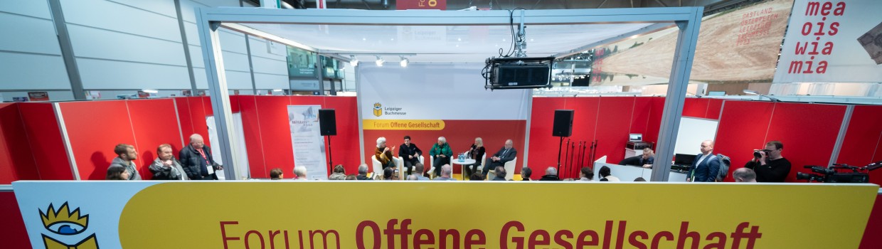 Das Forum Offene Gesellschaft der Leipziger Buchmesse von außen mit großem Schriftzug im Vordergrund. Im Hintergrund sieht man das Forum von innen während einer Diskussionsrunde.