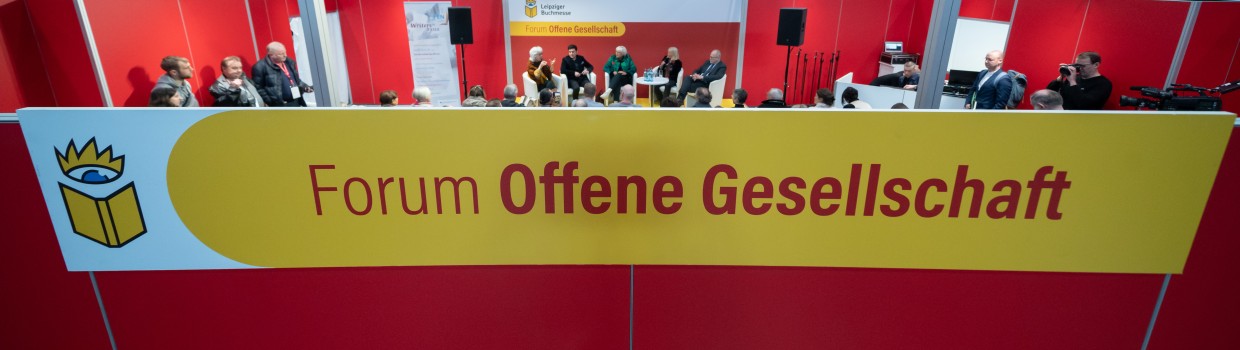 Das Forum Offene Gesellschaft der Leipziger Buchmesse von außen mit großem Schriftzug im Vordergrund. Im Hintergrund sieht man das Forum von innen während einer Diskussionsrunde.