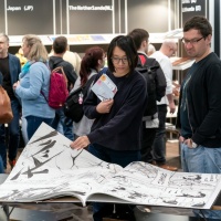 Besucher:innen blättern in einem riesigen illustrierten Buch im Buch- und Druckkunsbereich auf der Leipziger Buchmesse 2023 Besucher:innen blättern in einem riesigen illustrierten Buch im Buch- und Druckkunsbereich auf der Leipziger Buchmesse 2023