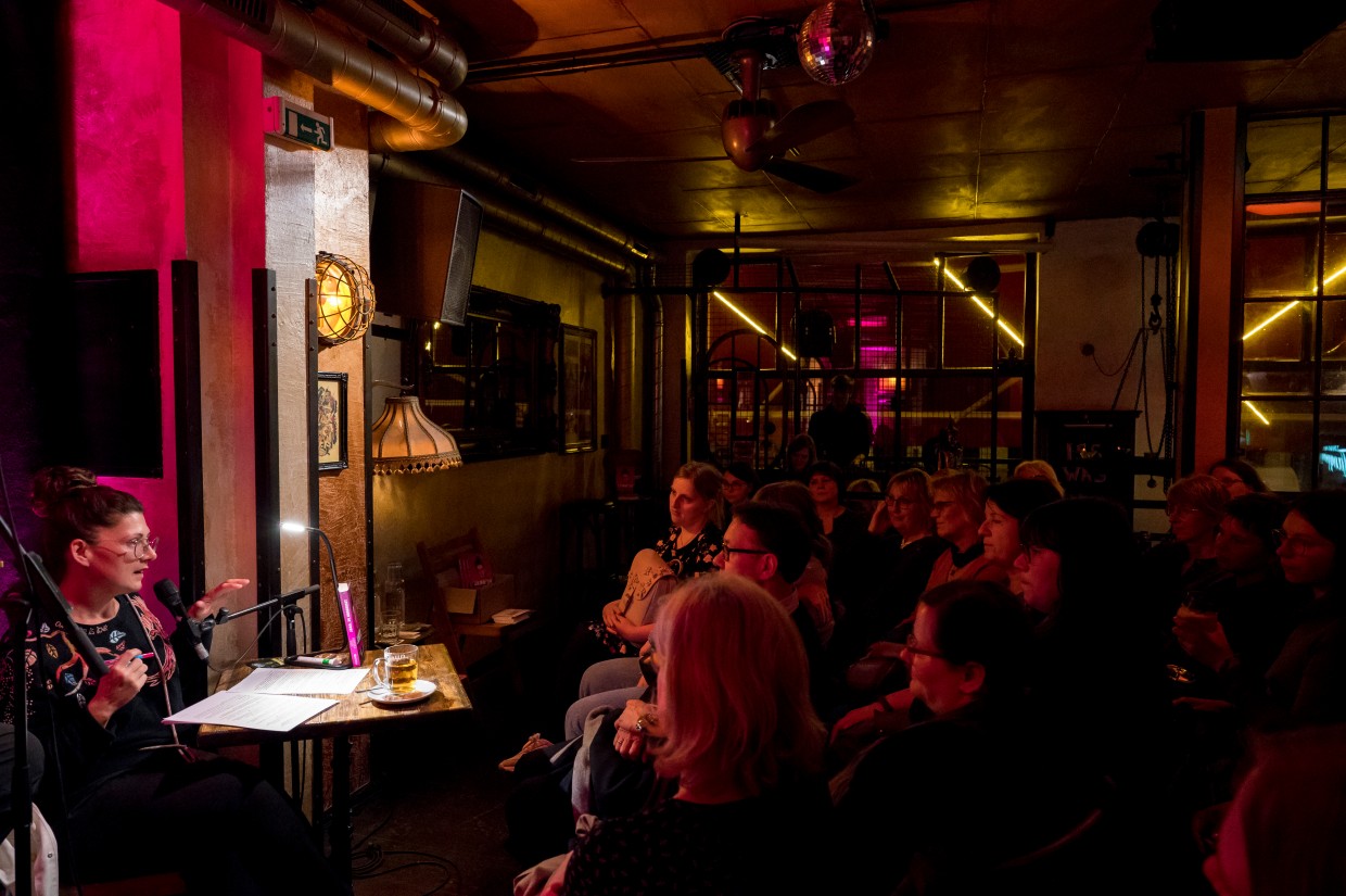 Aufnahme von Leipzig liest: Autorin Jana Crämer liest aus ihrem Buch am Mikrofon in einem vollbesetzten, abgedunkeltem Raum vor kleinem Publikum