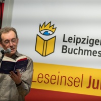 Ein Mann liest am Mikrofon aus einem Buch im Forum Leseinsel Junge Verlage auf der Leipziger Buchmesse 2023 Ein Mann liest am Mikrofon aus einem Buch im Forum Leseinsel Junge Verlage auf der Leipziger Buchmesse 2023