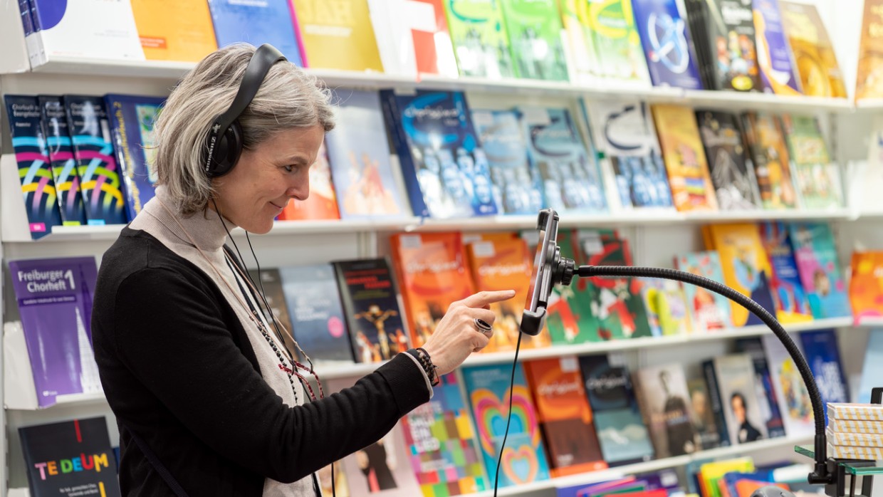 Besucherin mit Kopfhörern tippt auf ein Smartphone im Musikbereich während der Leipziger Buchmesse 2024