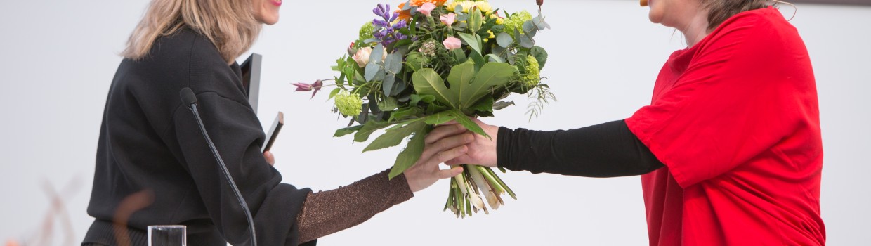 Jurorin Insa Wilke überreicht der Gewinnerin Barbi Marković einen Blumenstrauß am Rednerpult bei der Verleihung vom Preis der Leipziger Buchmesse 2024