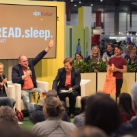 Bühnenveranstaltung des Podcasts "eat.read.sleep." mit mehreren Personen in der Audiowelt der Leipziger Buchmesse 2025 vor vollbesetztem Publikum