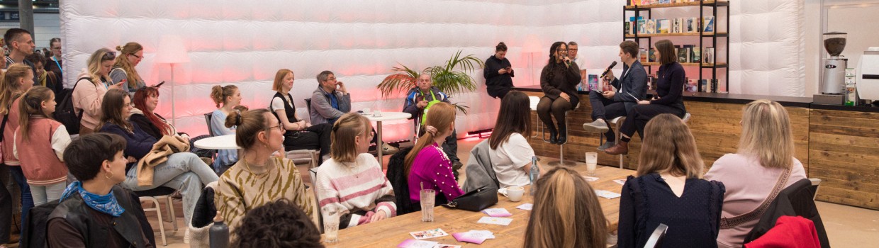 Eine Autorin im Gespräch mit den beiden Moderator:innen in der #buchbar während der Leipziger Buchmesse 2025 vor vollbesetztem Publikum Eine Autorin im Gespräch mit den beiden Moderator:innen in der #buchbar während der Leipziger Buchmesse 2025 vor vollbesetztem Publikum