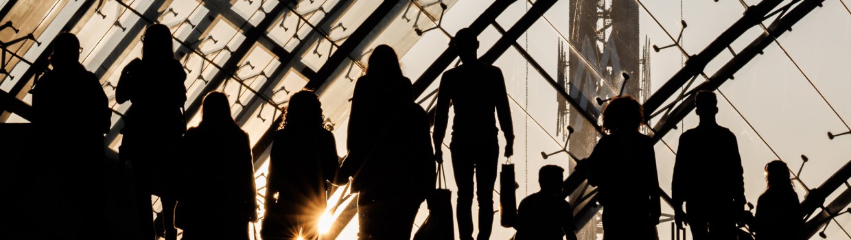 Dunkle Silhouette mehrerer Besucher:innen im Gegenlicht der untergehenden Sonne in der Glashalle der Leipziger Messe