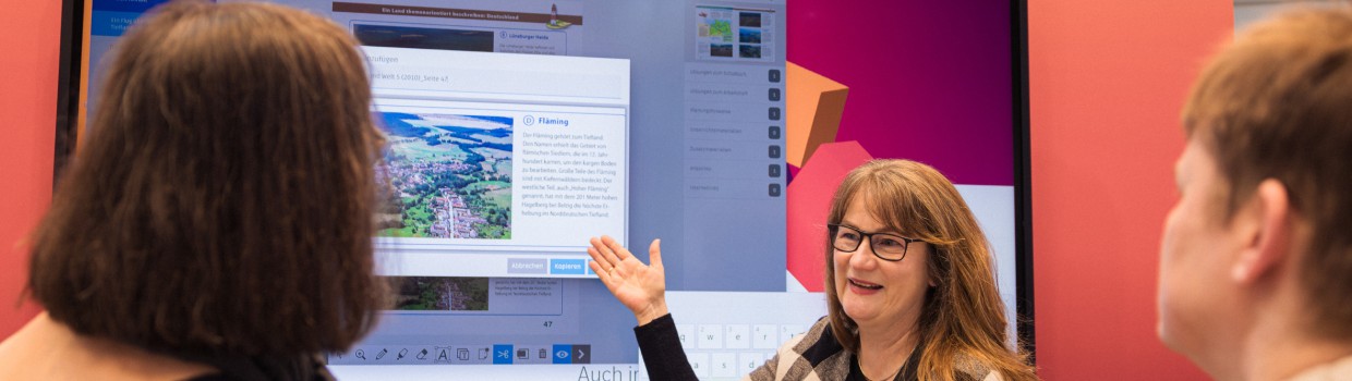 Ausstellerin im Bildungsbereich stellt auf der Leipziger Buchmesse 2025 mit Hilfe einer digitalen Wand zwei anderen Frauen ein Lernprogramm vor