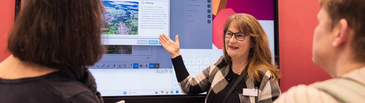Ausstellerin im Bildungsbereich stellt auf der Leipziger Buchmesse 2025 mit Hilfe einer digitalen Wand zwei anderen Frauen ein Lernprogramm vor