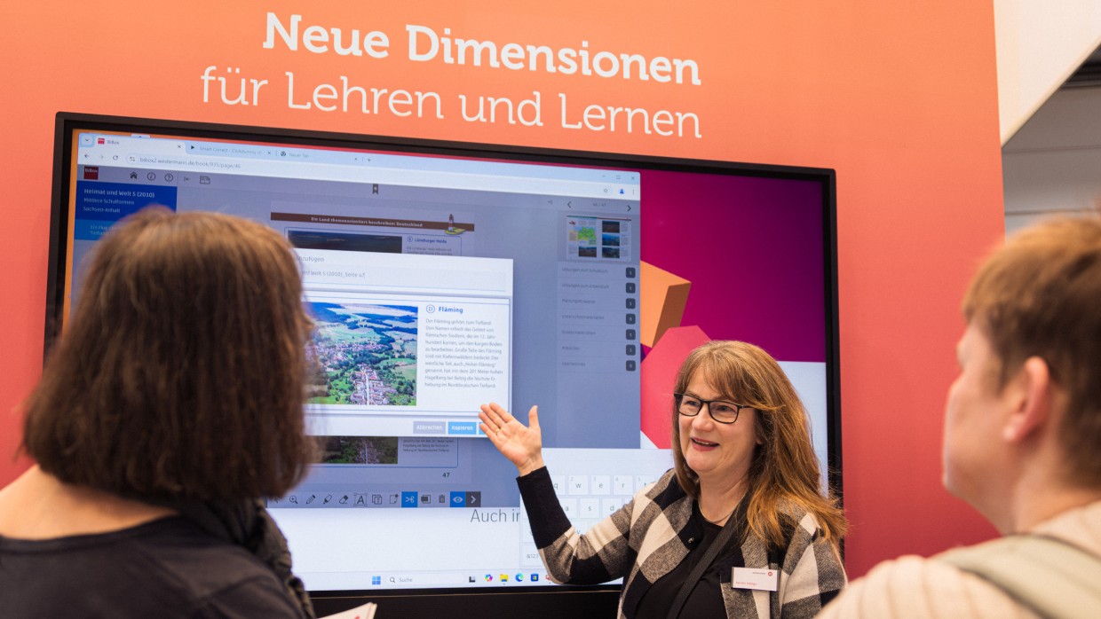 Ausstellerin im Bildungsbereich stellt auf der Leipziger Buchmesse 2025 mit Hilfe einer digitalen Wand zwei anderen Frauen ein Lernprogramm vor