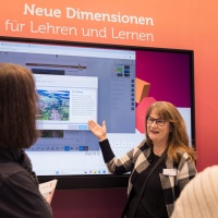 Ausstellerin im Bildungsbereich stellt auf der Leipziger Buchmesse 2025 mit Hilfe einer digitalen Wand zwei anderen Frauen ein Lernprogramm vor