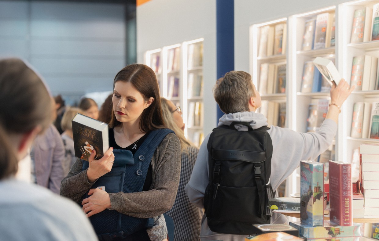 Eine Frau liest stehend in einem Buch vor einen großen Buchregal auf der Leipziger Buchmesse 2025