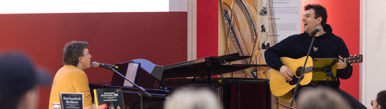 Das Musik-Café der Leipziger Buchmesse 2025 mit einer Bühnenveranstaltung von zwei Musikern an Gitarre und Klavierflügel vor vollbesetztem Publikum