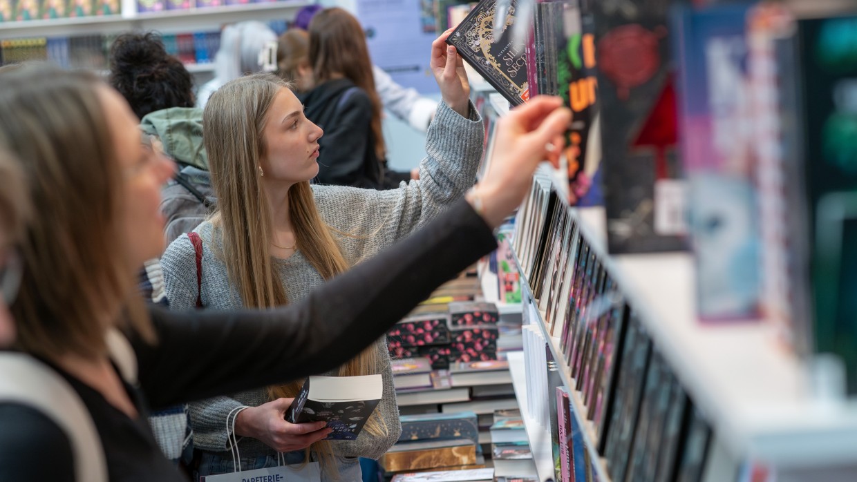 Frau nimmt sich ein Buch aus einem Regal auf der Leipziger Buchmesse 2025 Frau nimmt sich ein Buch aus einem Regal auf der Leipziger Buchmesse 2025