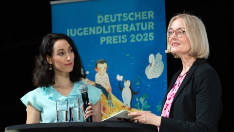 Moderatorin Vivian Perkovic und Prof. Dr. Iris Kruse im Gespräch auf der Bühne des Jugendliteraturpreises 2025 Moderatorin Vivian Perkovic und Prof. Dr. Iris Kruse im Gespräch auf der Bühne des Jugendliteraturpreises 2025