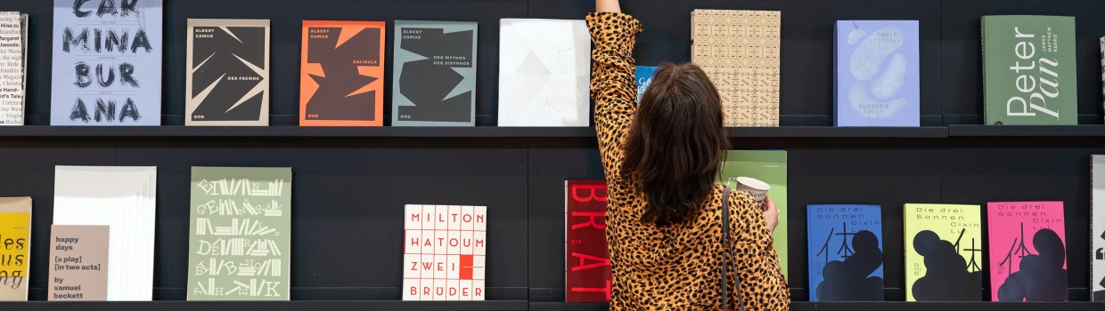 Besucherin der Leipziger Buchmesse 2025 nimmt ein Buch aus einer Wand mit ausgestellten Büchern