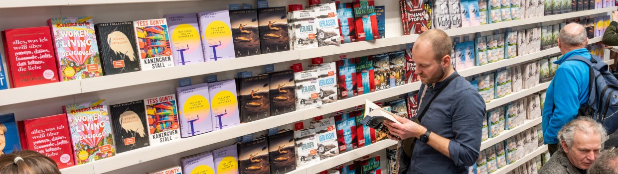 Ein Mann liest stehend in einem Buch vor einen großen Buchregal auf der Leipziger Buchmesse 2025 Ein Mann liest stehend in einem Buch vor einen großen Buchregal auf der Leipziger Buchmesse 2025