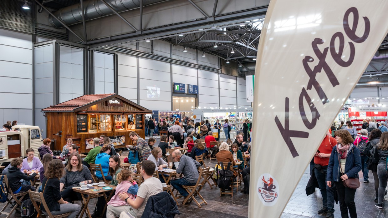 Einer der gastronomischen Bereiche in der Messehalle der Leiziger Buchmesse 2025 mit vielen Besucher:innen an Tischen und einem Verkaufsstand im Hintergrund Einer der gastronomischen Bereiche in der Messehalle der Leiziger Buchmesse 2025 mit vielen Besucher:innen an Tischen und einem Verkaufsstand im Hintergrund