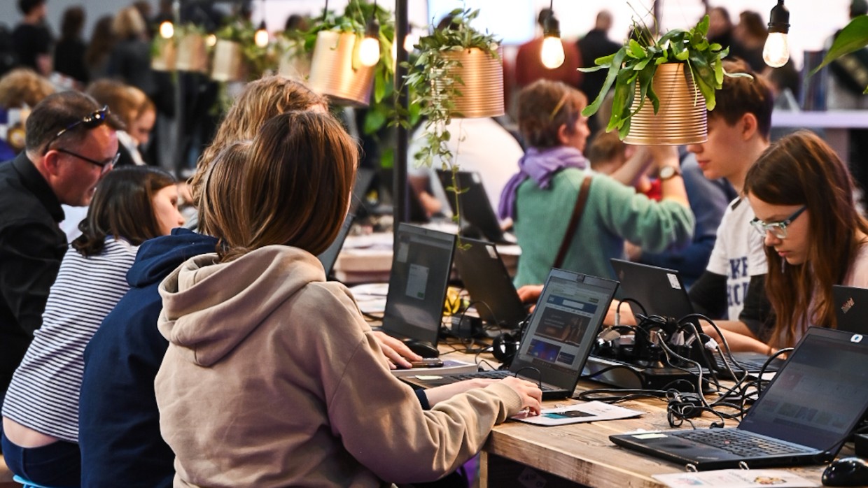 In der Hacker School im UVERSE auf der Leipziger Buchmesse 2025 sitzen Kinder an langen Tischen und arbeiten an Laptops