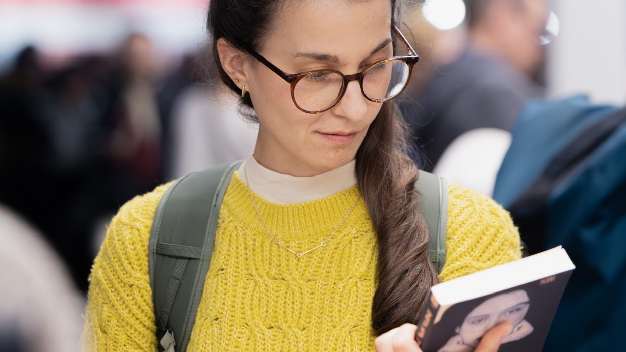 Eine Frau in gelbem Pullover betrachtet ein Buch auf der Leipziger Buchmesse 2026