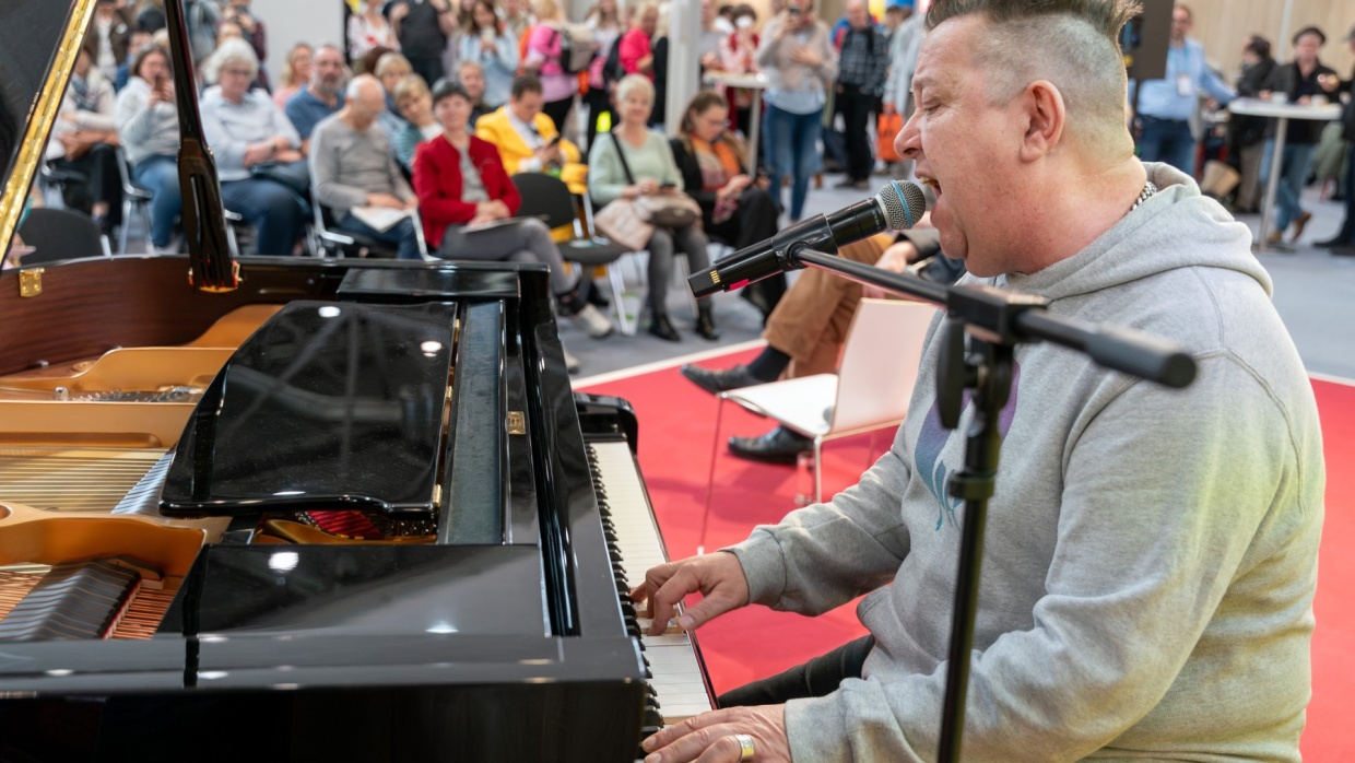 Sebastian Krumbiegel singt und spielt am Piano auf einer Bühne vor vollbesetztem Publikum auf der Leipziger Buchmesse 2026