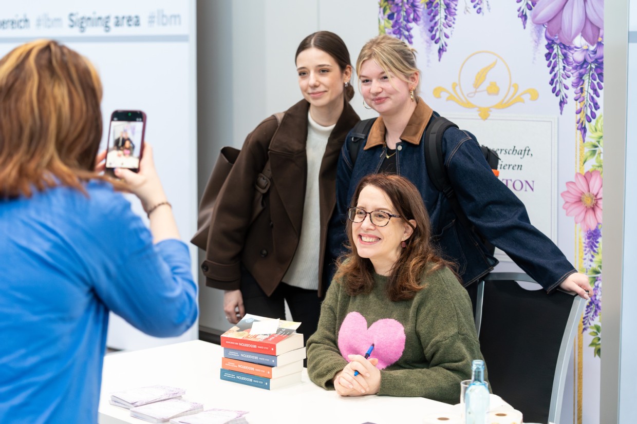 Autorin Julia Quinn posiert mit zwei Besucherinnen am Signiertisch der Leipziger Buchmesse 2026 für ein Foto