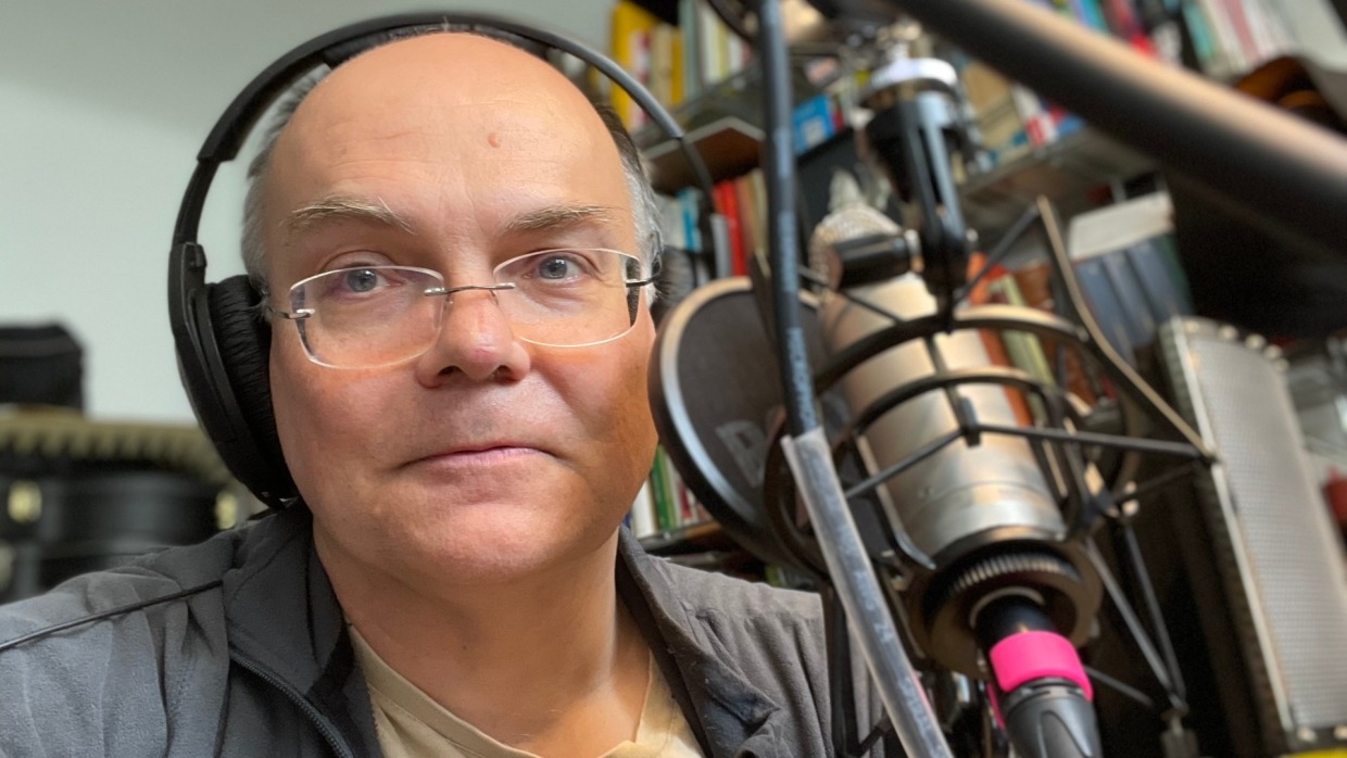 Photograph of Stephan Ozsváth wearing headphones in front of a large microphone in his office