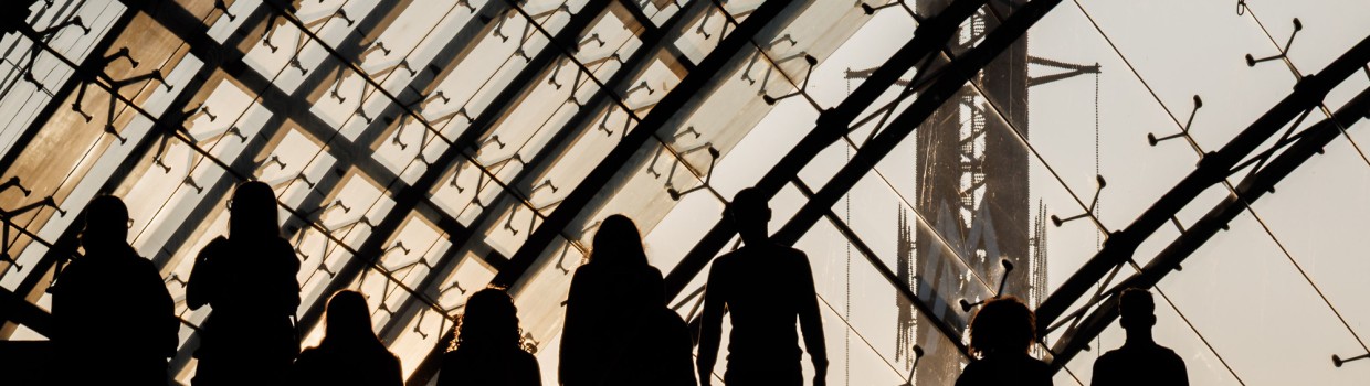 Dark silhouettes of several visitors against the backdrop of the setting sun in the glass hall of the Leipzig Trade Fair