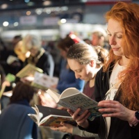 Woman with red curly hair reading from a book at the Leipzig Book Fair 2025