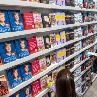 Colorful bookshelf with many books, in front of which visitors to the Leipzig Book Fair 2025 stand and read