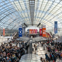 Interior view of the glass hall at Leipzig Exhibition Center with colorful banners and many visitors at the Leipzig Book Fair 2025