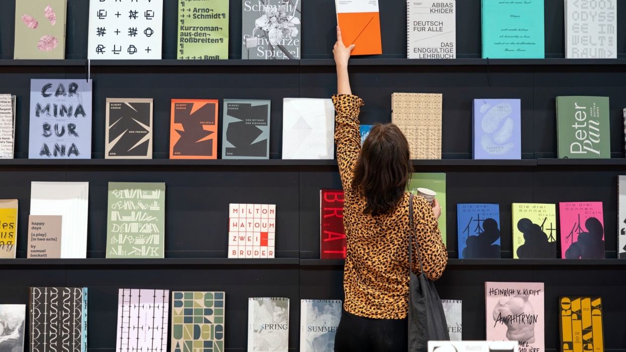 A visitor to the Leipzig Book Fair in 2025 takes a book from a wall displaying books