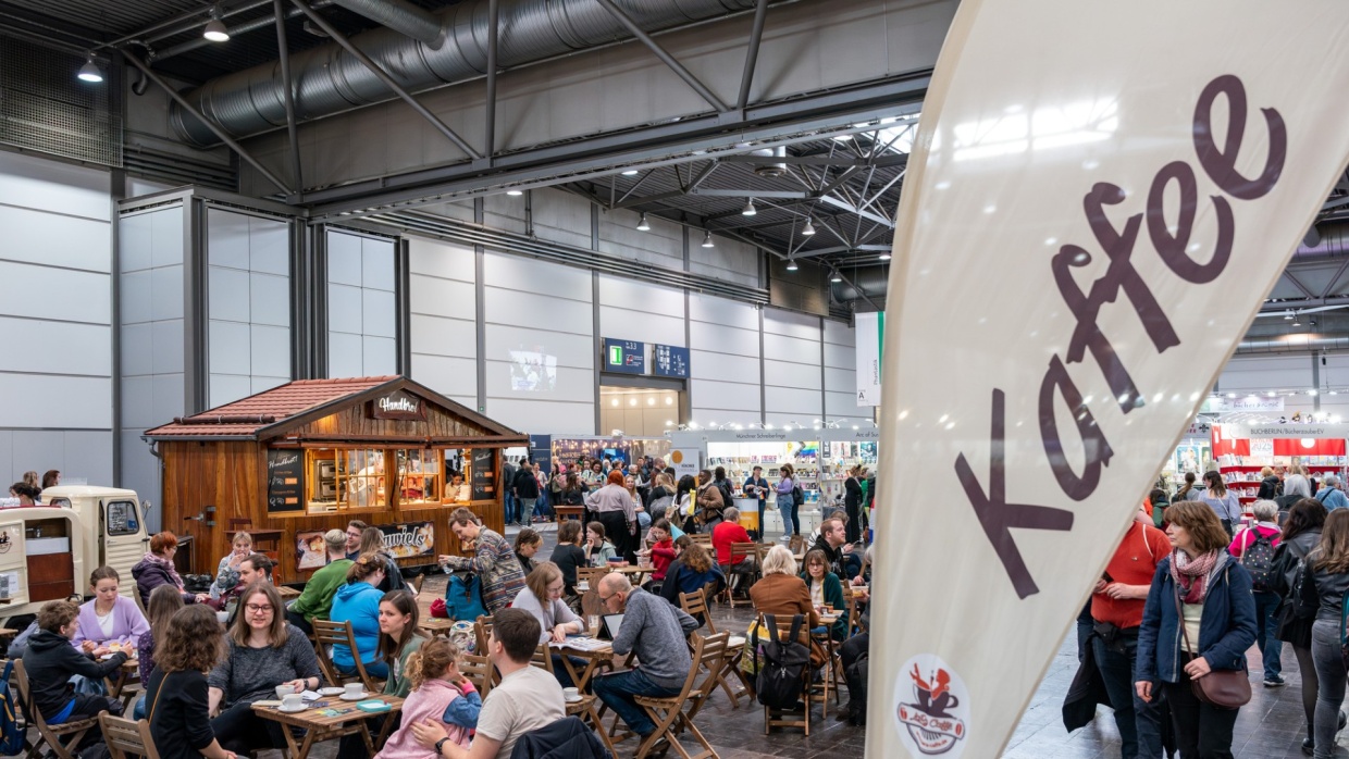 One of the food courts in the exhibition hall at the 2025 Leipzig Book Fair, with many visitors seated at tables and a sales stand in the background
