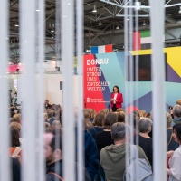Christina Beinhoff speaking on stage in front of a big audience at the trade fair stand of the Focus Topic Danube at Leipzig Book Fair 2026