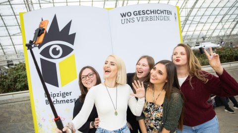 Five young female visitors take a selfie in front of a large book fair display at Leipzig Book Fair 2026